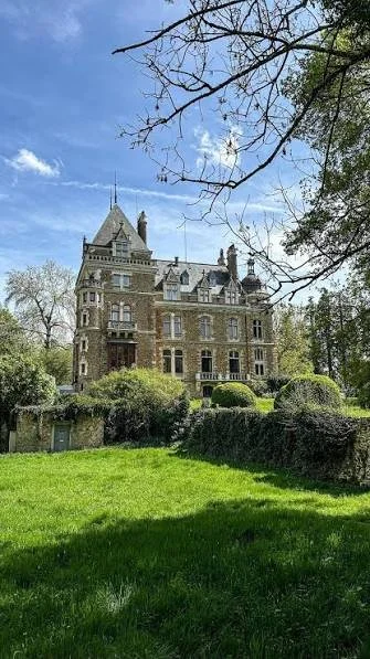 A large, historic castle-like building surrounded by trees and greenery on a sunny day.