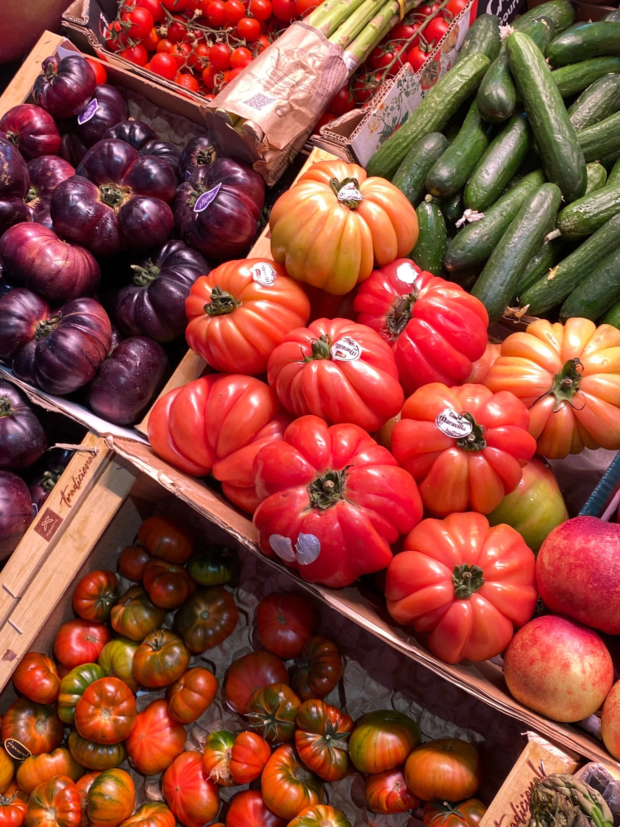 A display of heirloom tomatoes, cucumbers, cherry tomatoes, and zucchini in a grocery store produce section.