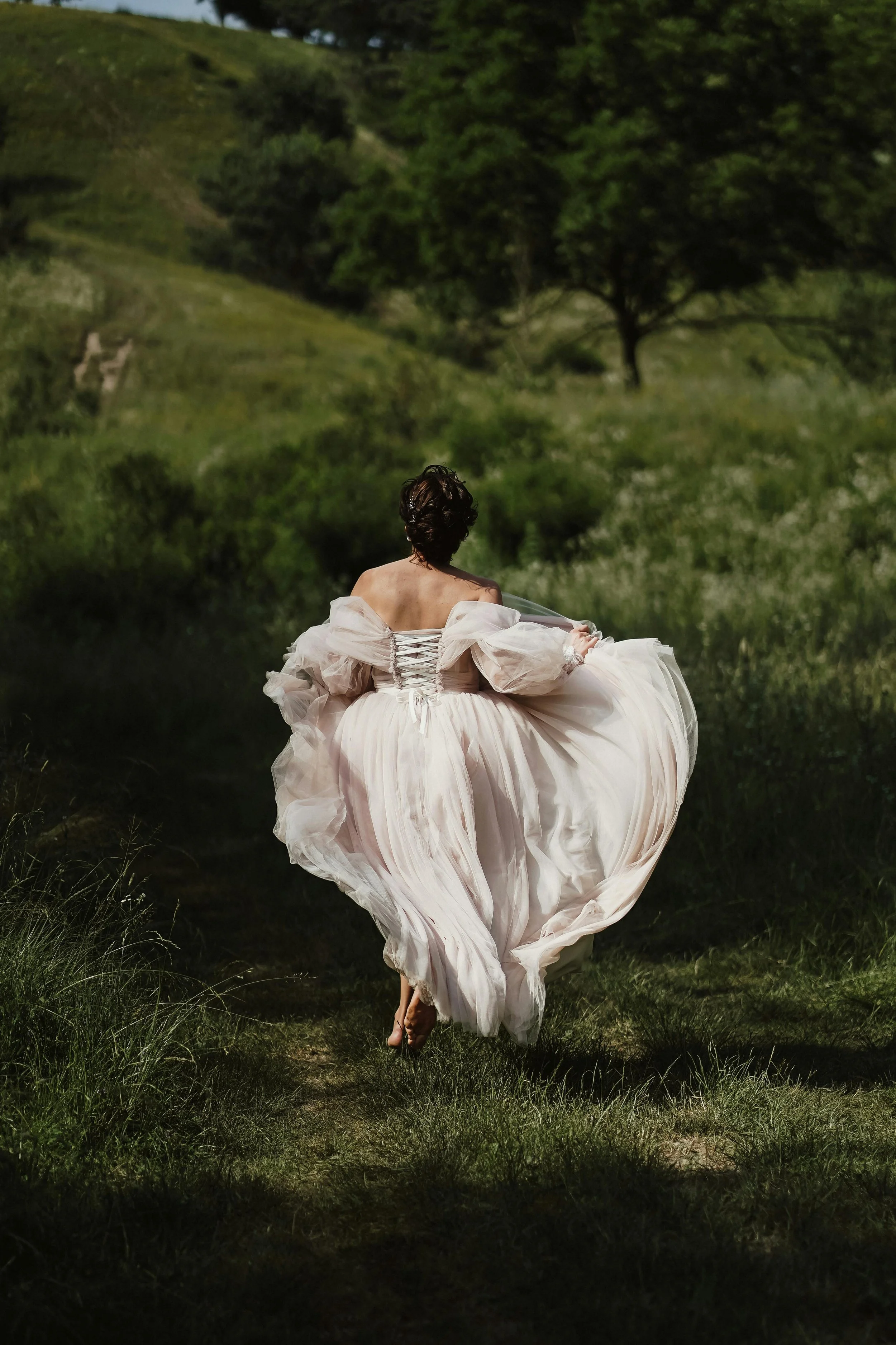 A person wearing an elegant white dress runs through a grassy field with trees in the background.