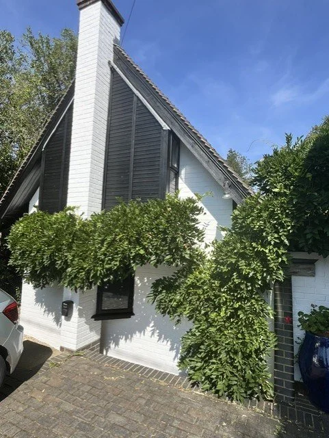 Front elevation of the Bridge House in Bicknacre with restored white brickwork, black exterior woodwork finished in Sadolin Obsidian, and detailed decorating around the chimney, windows and fascia boards.