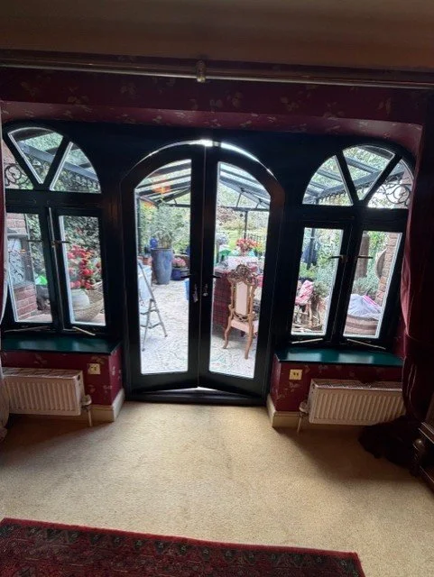 The newly painted dark green patio doors and surrounding windows, replacing the previous white finish. A key part of this dining room renovation, bringing the woodwork together with the newly decorated walls and ceiling.