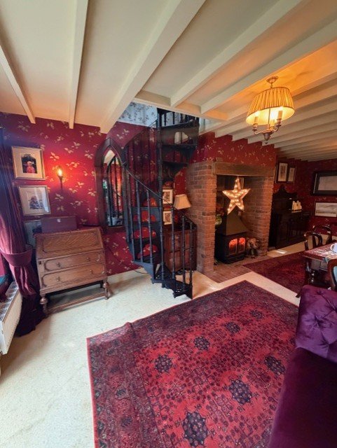 A wider view of the dining room, showcasing the patterned wallpaper and freshly painted ceiling beams alongside the existing brick fireplace and spiral staircase. Part of a complete interior redecoration in Tollesbury, Essex.