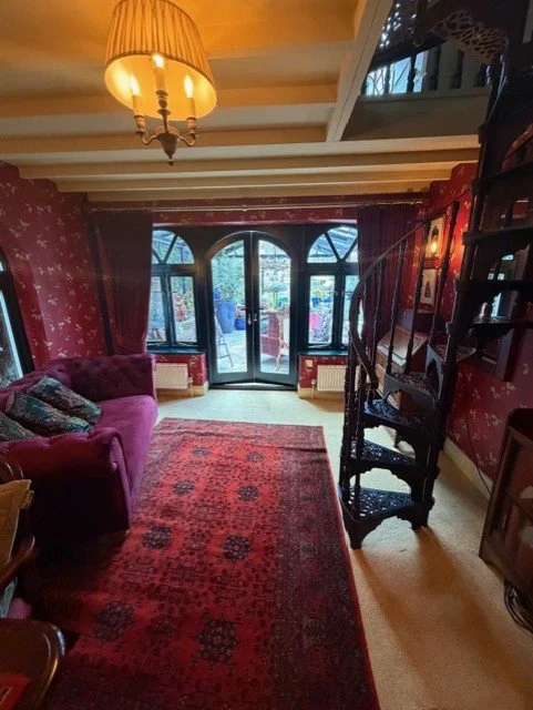 A view across the redecorated dining room towards the garden. The project included wallpapering the walls, painting the ceiling and beams, and changing the window and door frames from white to dark green.