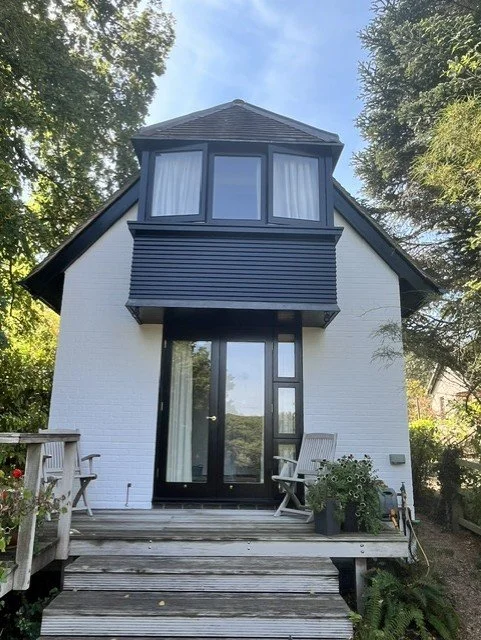 Rear entrance elevation completed as part of a full exterior refurbishment in Bicknacre, including white masonry, black timber cladding, exterior doors, windows and decorative detailing throughout.