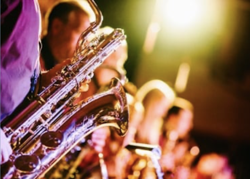 Close-up of saxophones being played by musicians in a band during a live performance with colorful stage lighting.