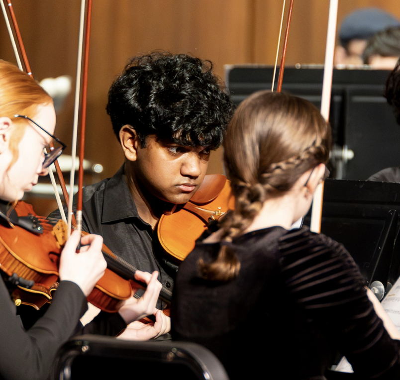 Young musicians in an orchestra playing violins, focusing intently on their sheet music.