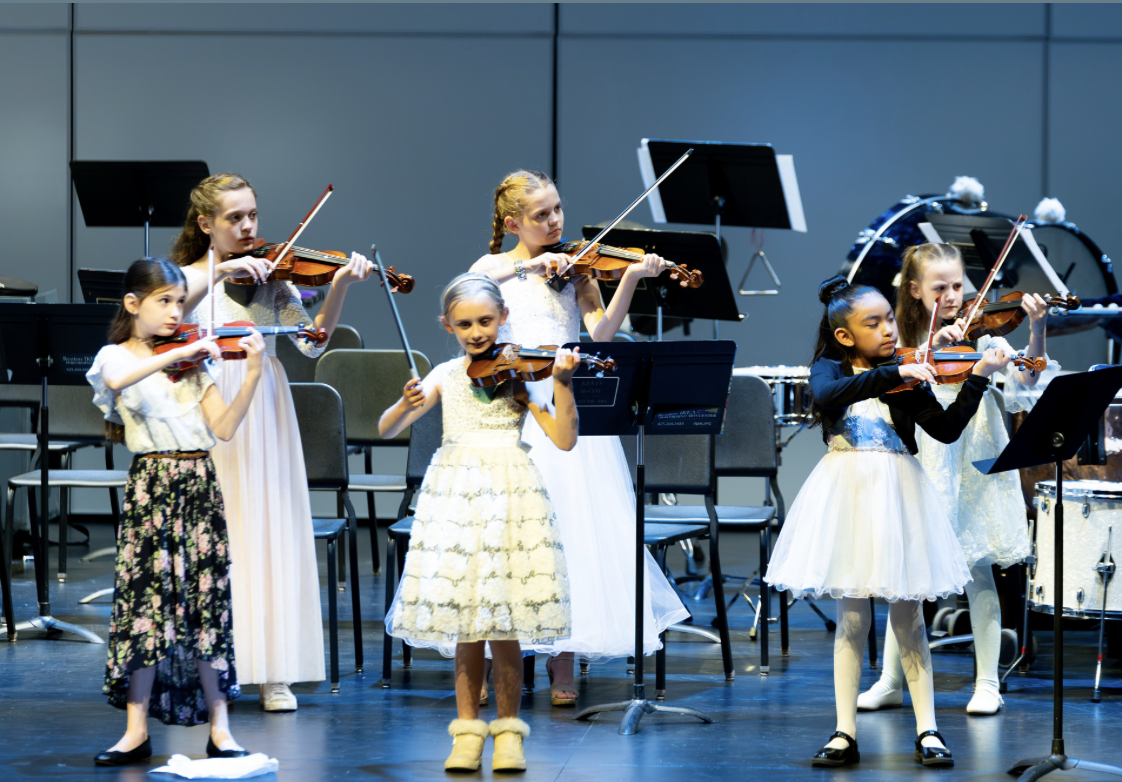 Young girls playing violins during a musical performance on stage.