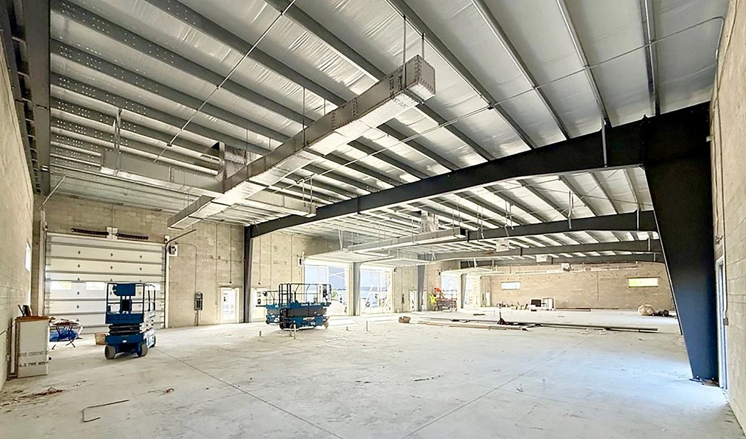 Interior of a large warehouse under construction with exposed beams, lifts, and construction materials.
