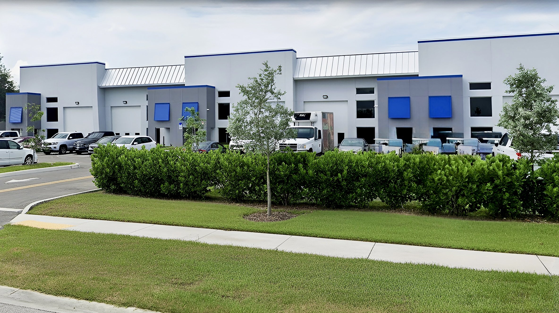 A commercial building with a parking lot, trees, and shrubs in the foreground.
