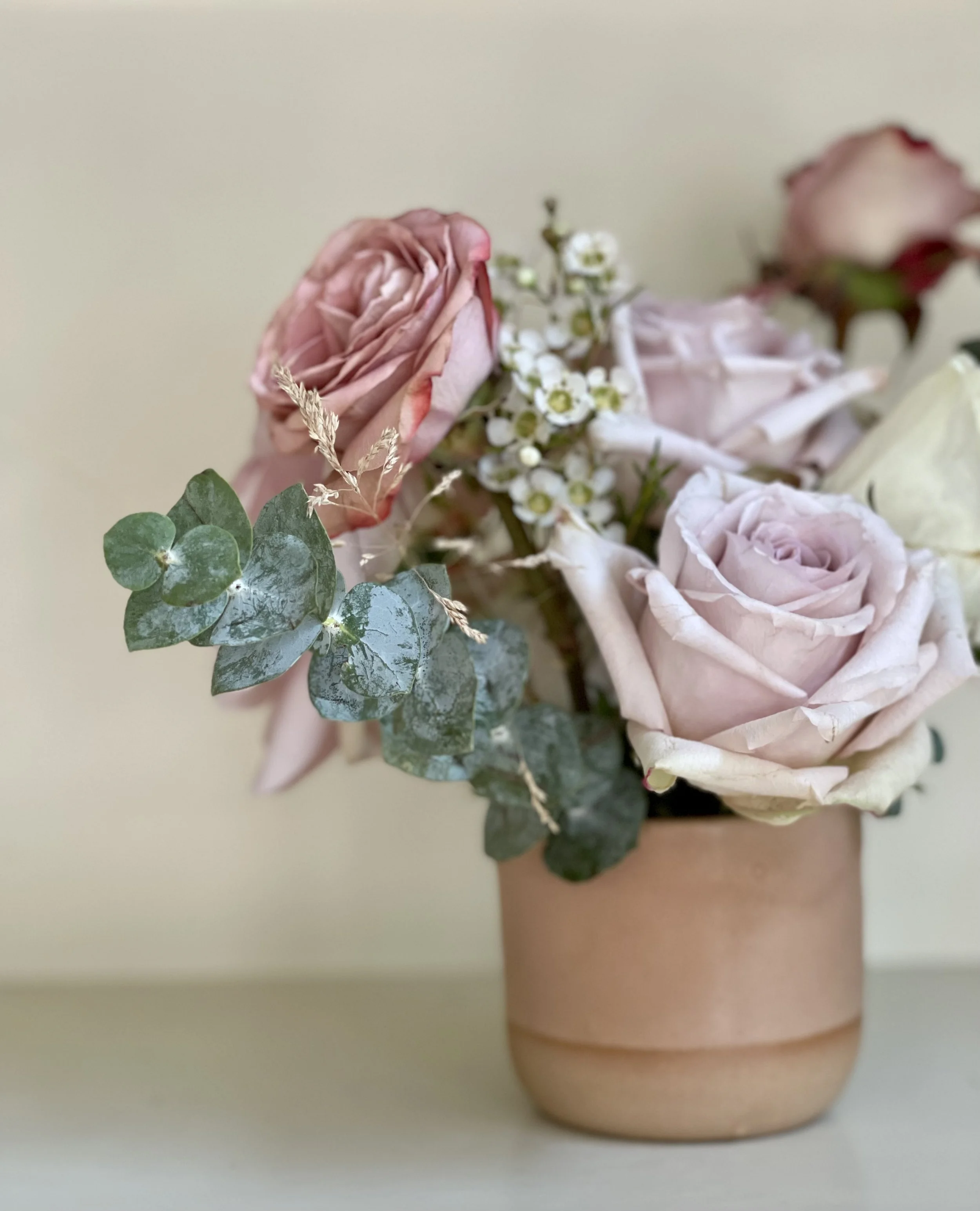 A vase with pink roses, white roses, small white flowers, and green leaves on a neutral background.
