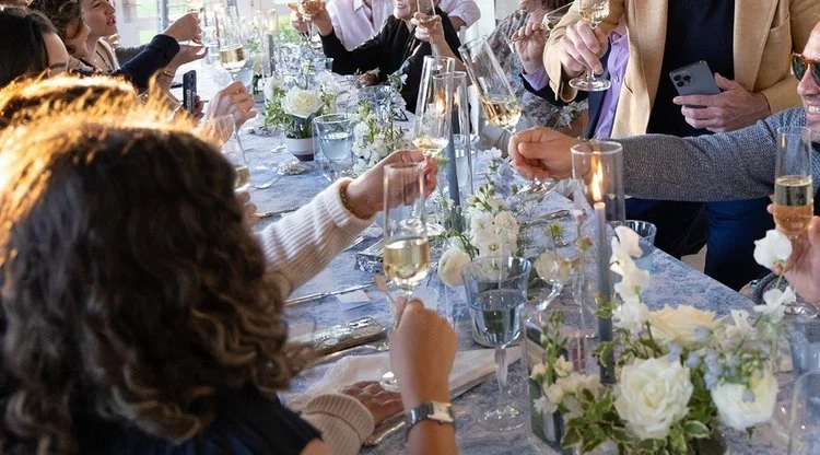 People gathered around a table celebrating with toasts, champagne glasses, and floral centerpieces.