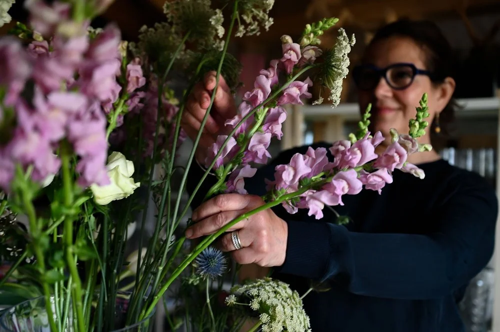 A woman arranging pastel pink and white flowers in a floral shop.