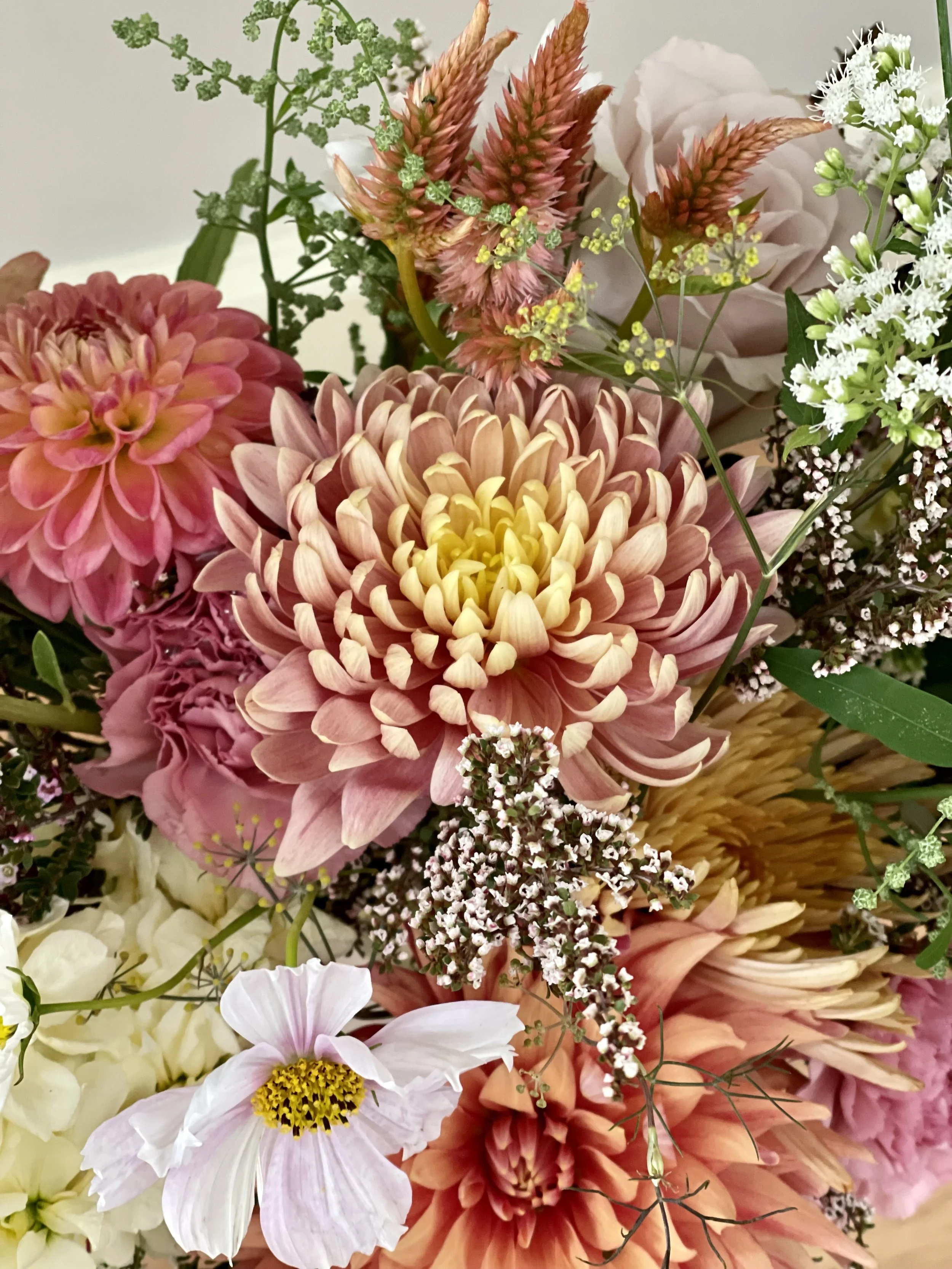 A vibrant bouquet of various flowers including dahlias, cosmos, and other blossoms in shades of pink, peach, cream, and white.