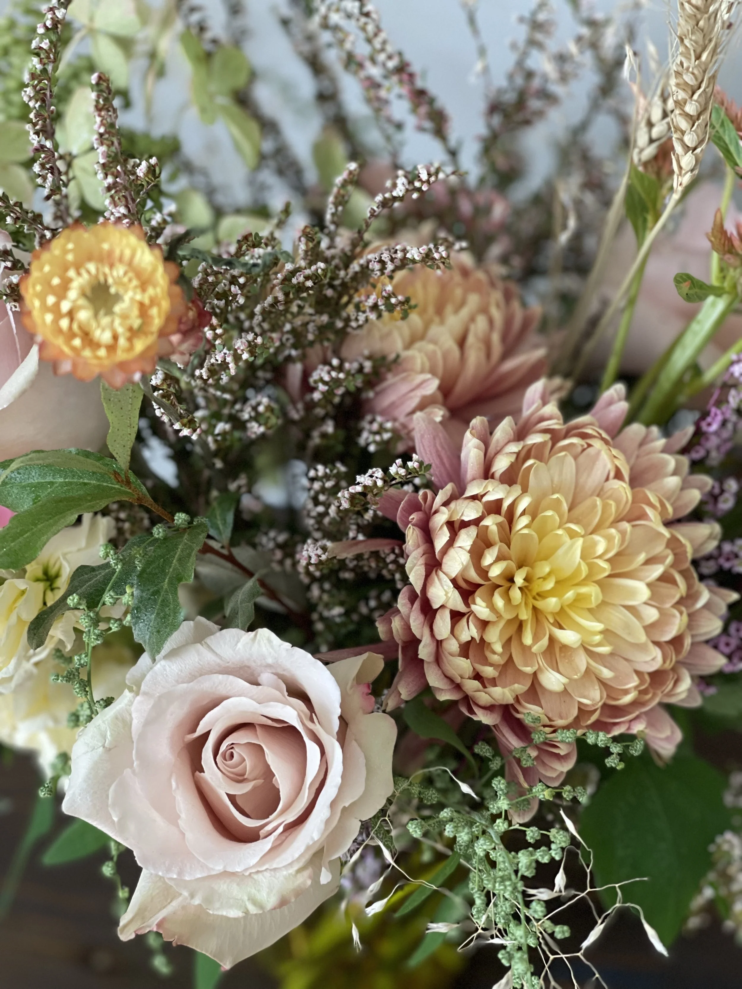 Close-up of a bouquet with pink roses, peach dahlia, small white and purple flowers, and green foliage.