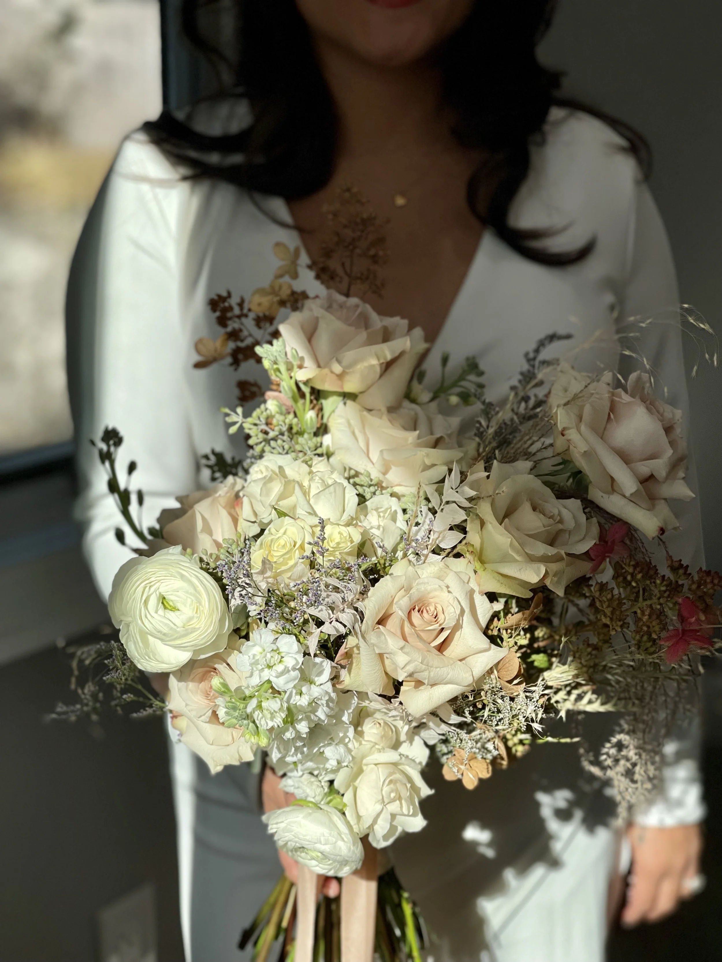 Woman holding a large bouquet of light-colored roses, ranunculus, and greenery.