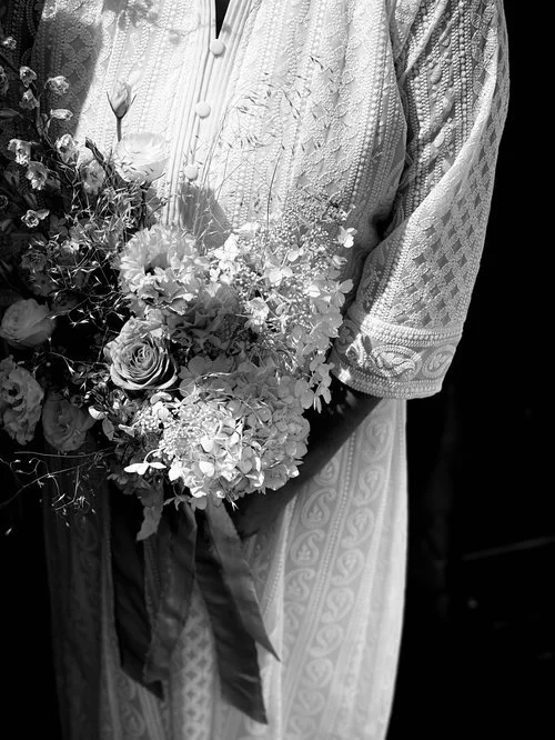 Close-up of a woman wearing a detailed embroidered dress, holding a large bouquet of flowers.