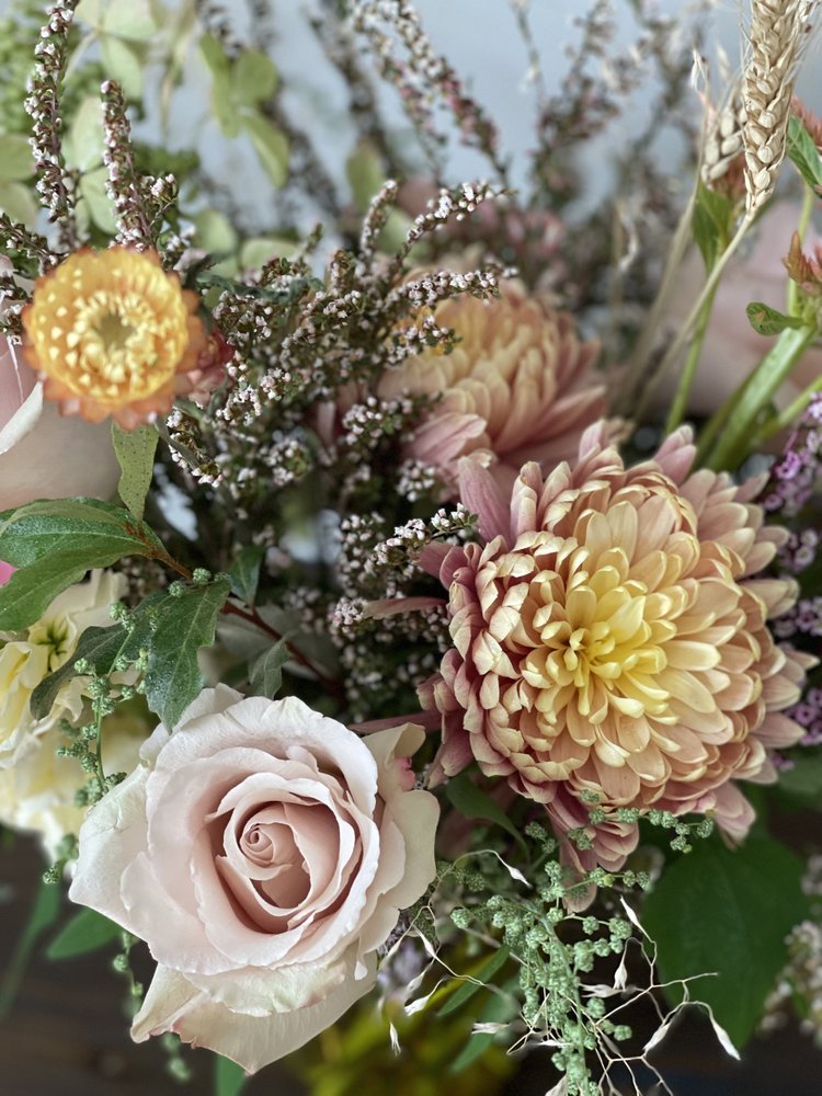 A close-up of a bouquet with pink roses, peach-colored dahlias, small purple and white flowers, and greenery.
