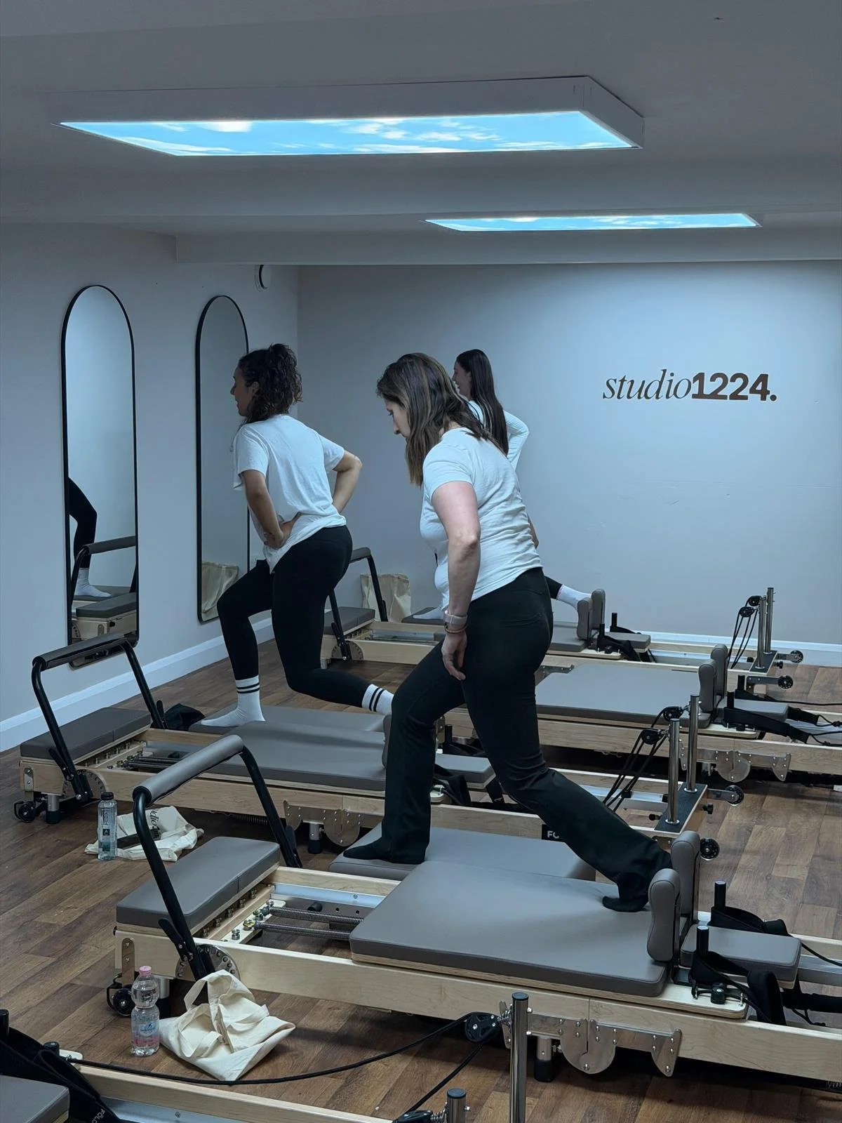 Three women using Pilates reformer machines in a studio labeled 'studio1224'.