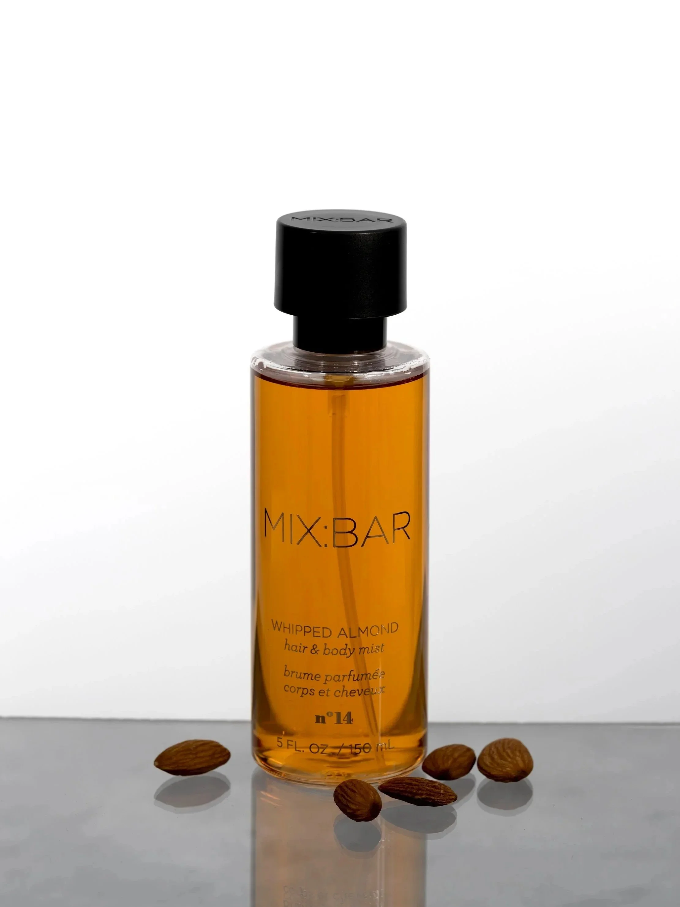 Bottle of MIX:BAB whipped almond hair and body mist with almonds placed in front of it on a reflective surface.