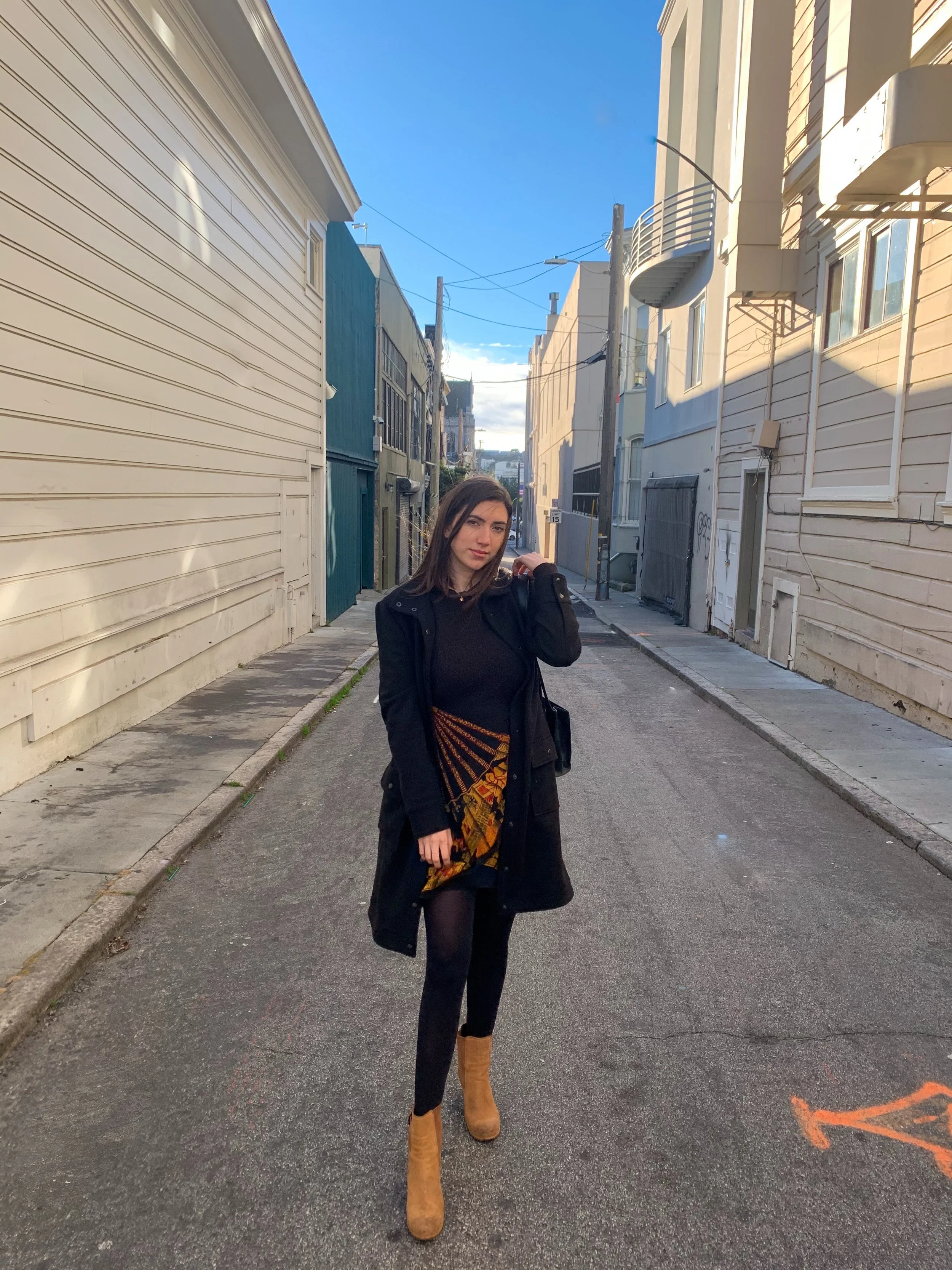 A woman standing in the middle of a narrow alleyway with colorful buildings on either side under a blue sky.