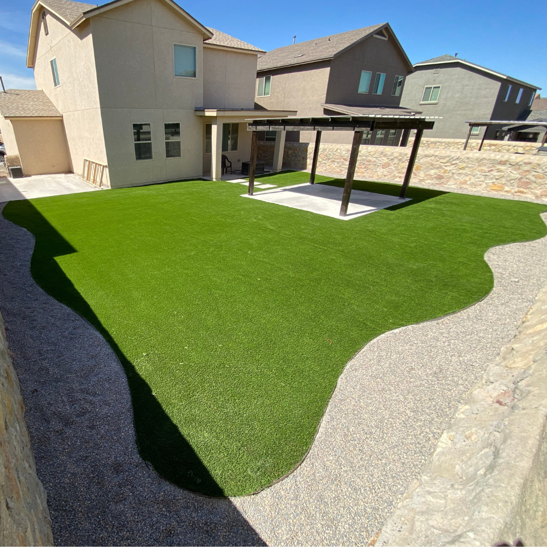 Backyard with artificial grass, beside a concrete pathway and a home with a covered patio and outdoor furniture.