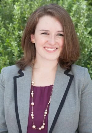Democrat Molly McKee-Seabrook for Maryland house of Delegates in District 22, with shoulder-length brown hair smiling, wearing a gray blazer over a purple top, with a pearl necklace, outdoors with greenery in the background.