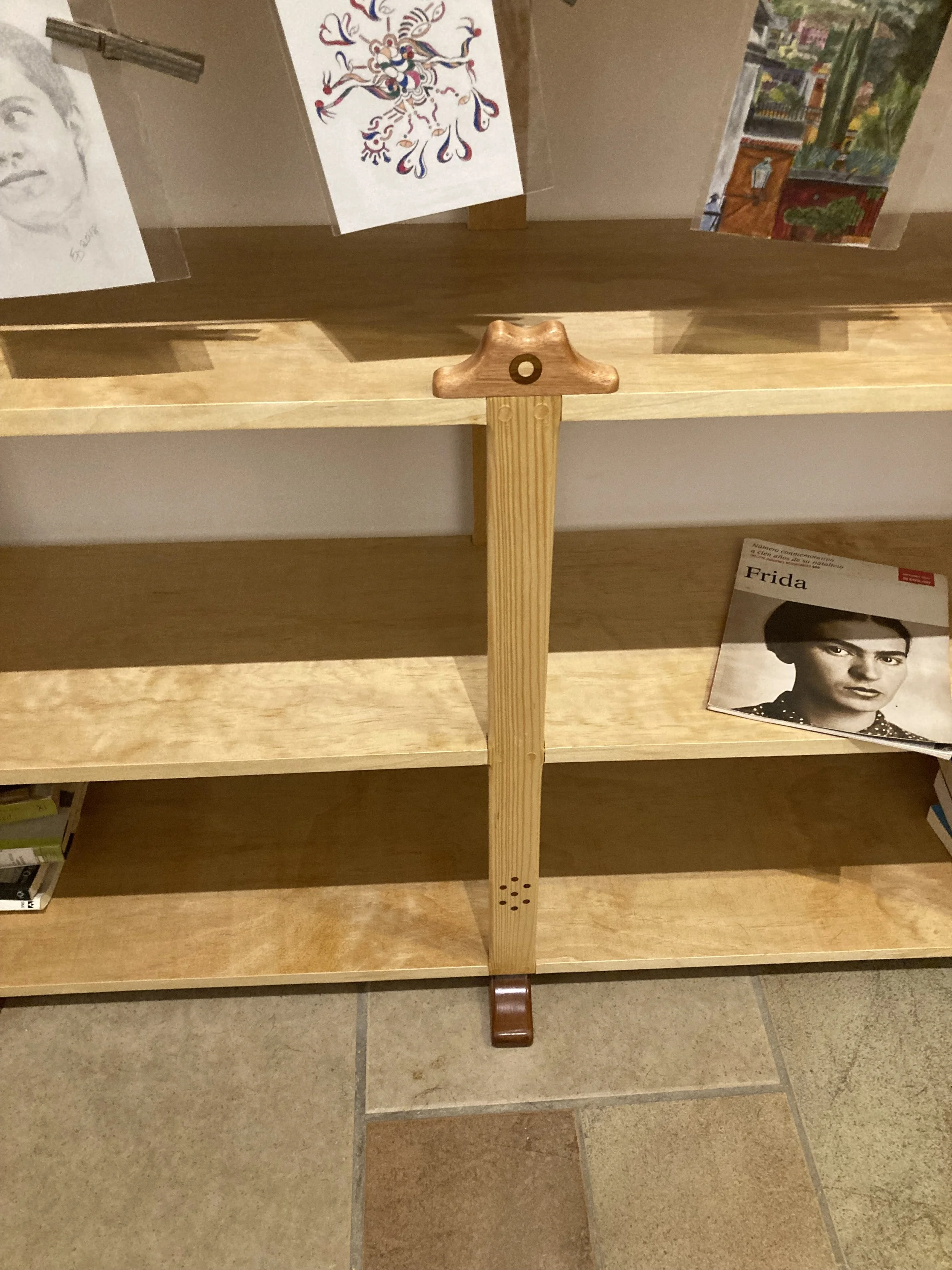 Wooden bookshelf with artwork and a magazine titled 'Frida' on the shelf.