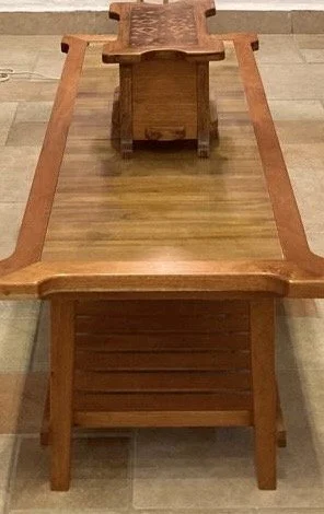 A wooden table turned upside down, with a smaller wooden object placed on top of it, all on a wooden floor.