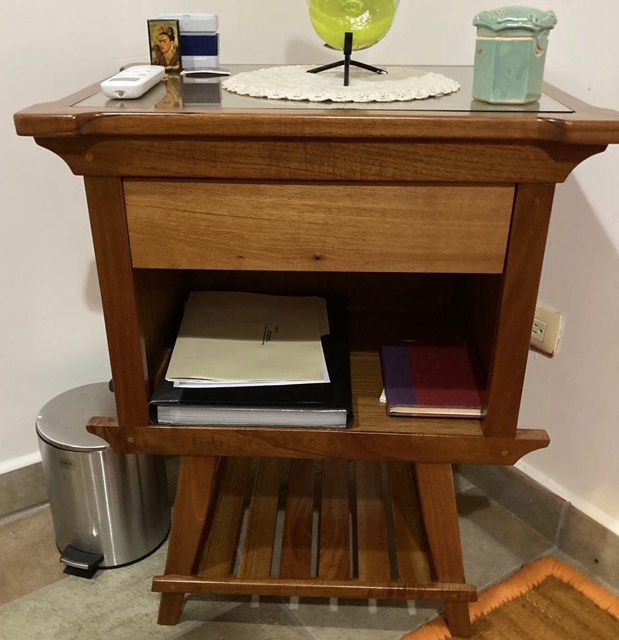 Wooden side table with books and decorative items on top, next to a stainless steel trash can and a beige rug.
