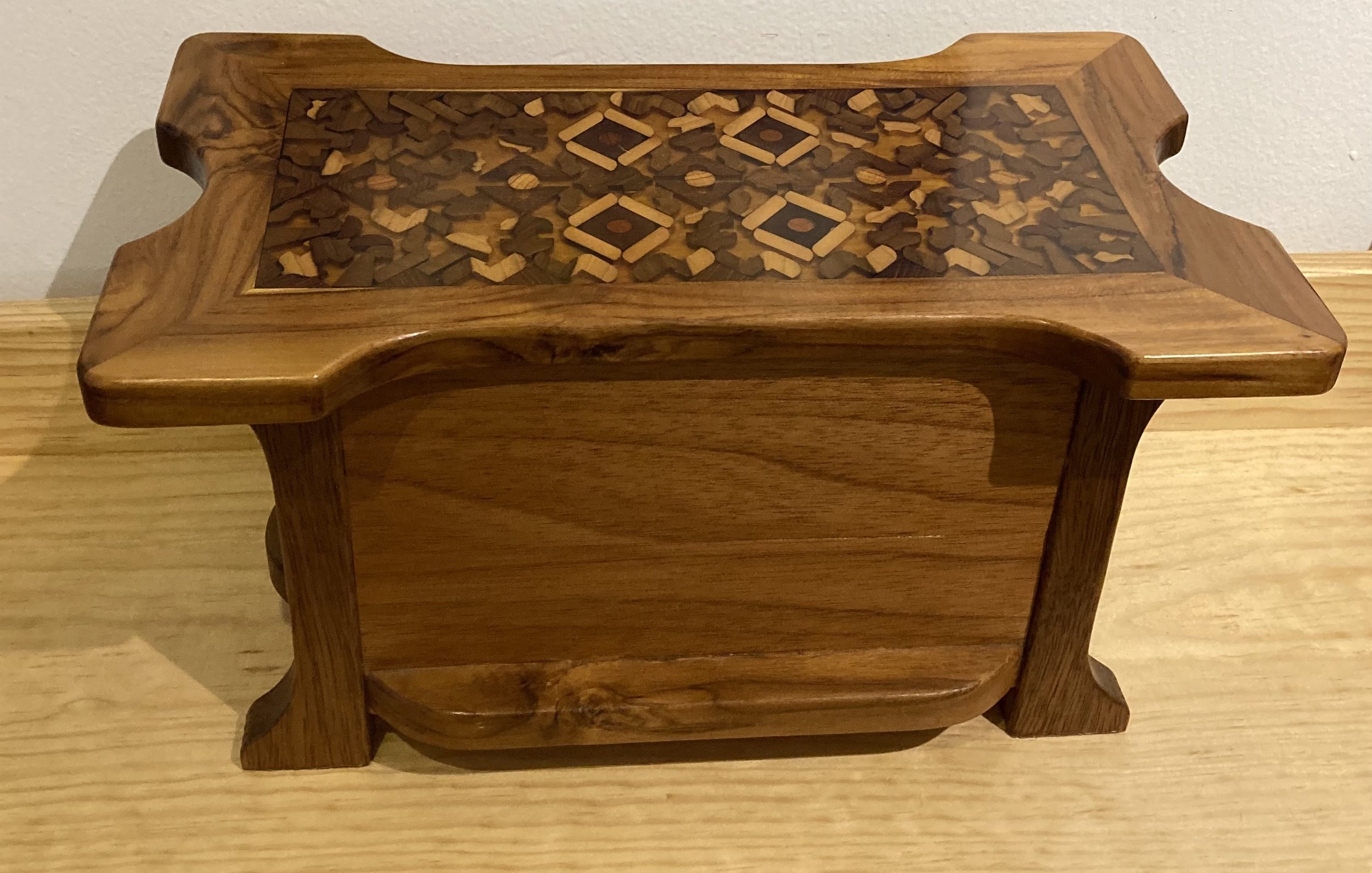 A wooden box with intricate inlay pattern on the top, sitting on a wooden surface.