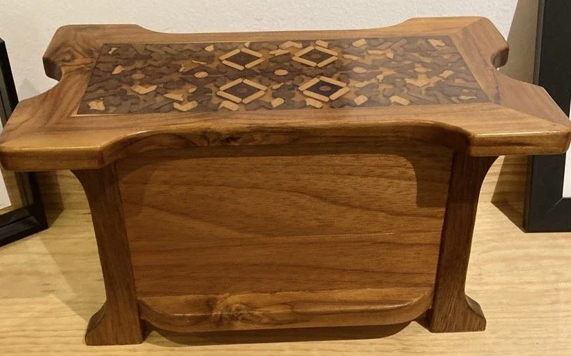 A wooden table with an intricate inlay design on the top surface, featuring geometric patterns in contrasting wood tones.