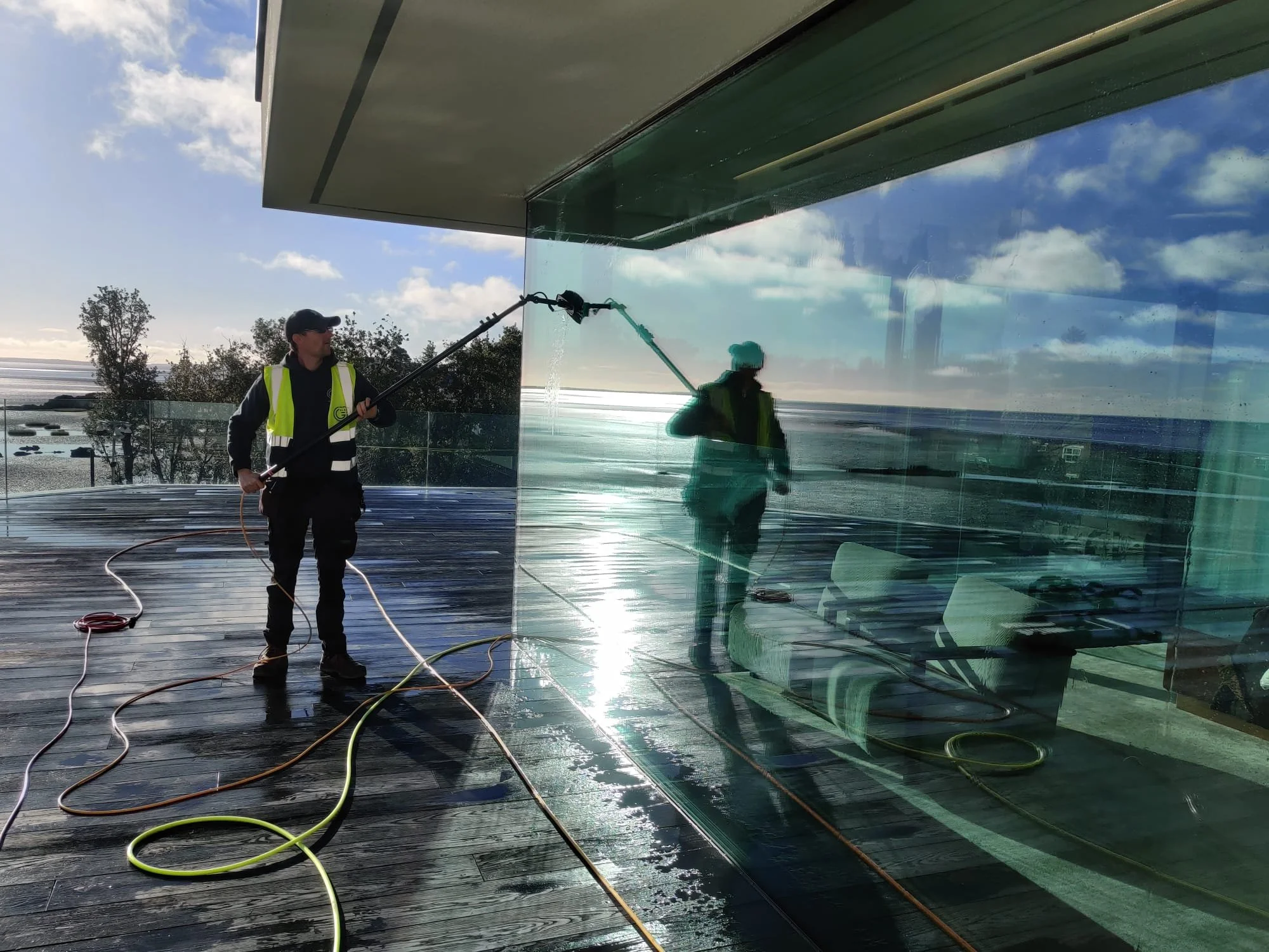 Professional window cleaner in Dundalk using a water-fed pole system to clean large exterior glass windows on a modern residential property.