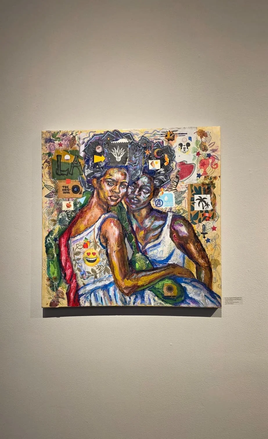 A colorful painting of two women with natural hair, sitting close together, surrounded by various symbols and patterns, with a collage background.