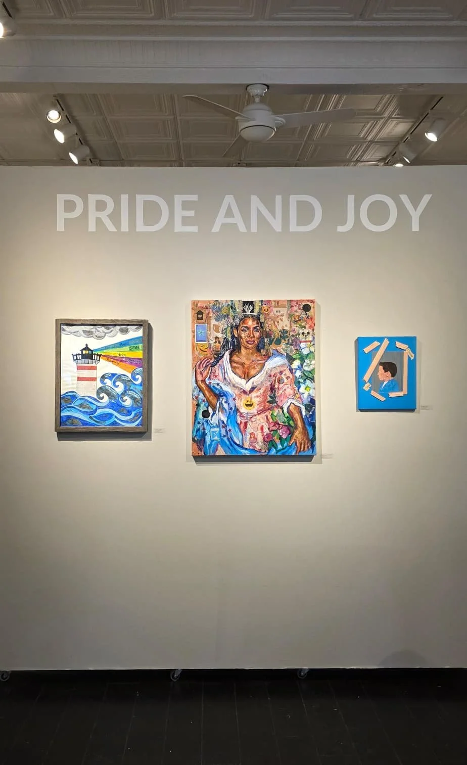 An art gallery wall displaying three colorful artworks with the phrase "PRIDE AND JOY" above them.