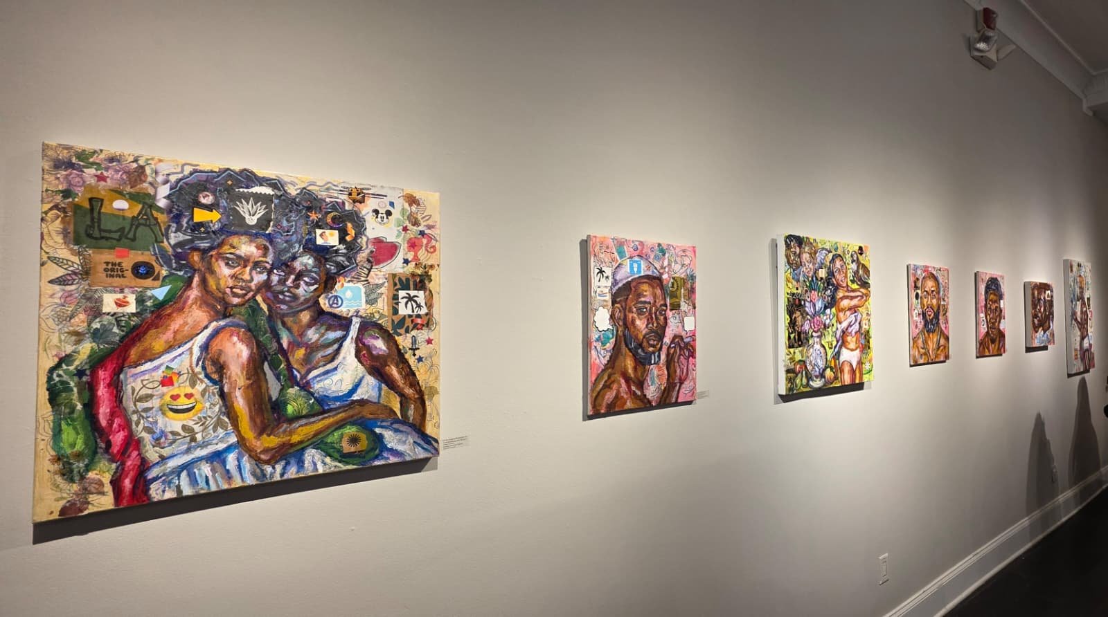 Colorful art gallery display with six paintings of diverse black individuals on a white wall.