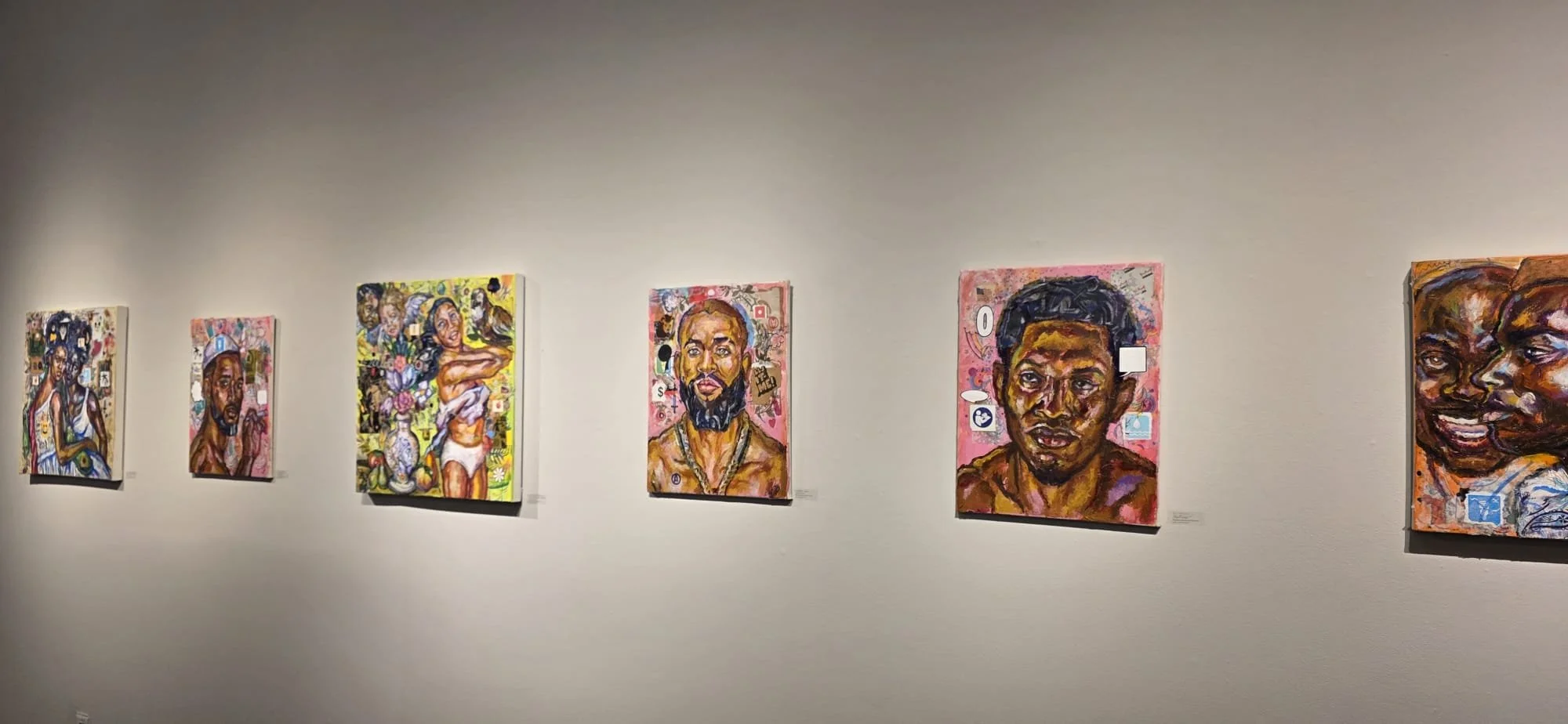 Gallery of colorful portraits of diverse people displayed on a white wall in an art exhibit.
