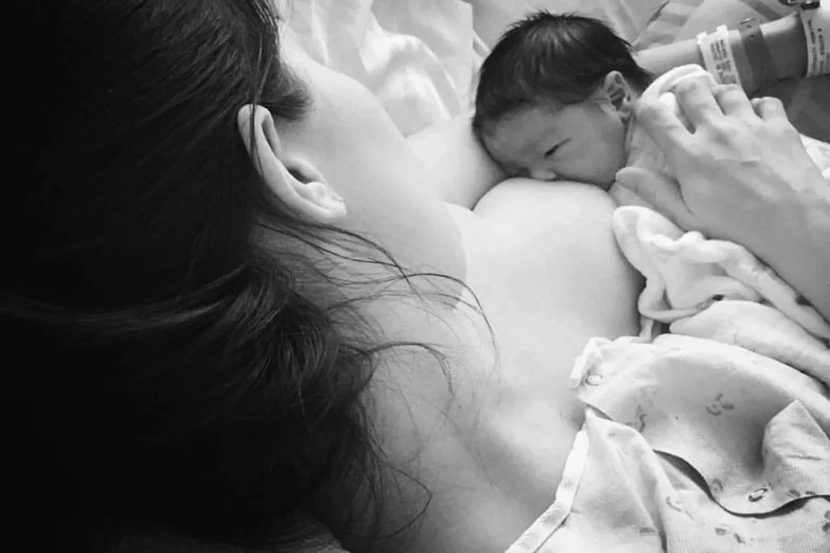 A woman breastfeeding a newborn baby in a hospital room, with medical tubes attached to the baby.