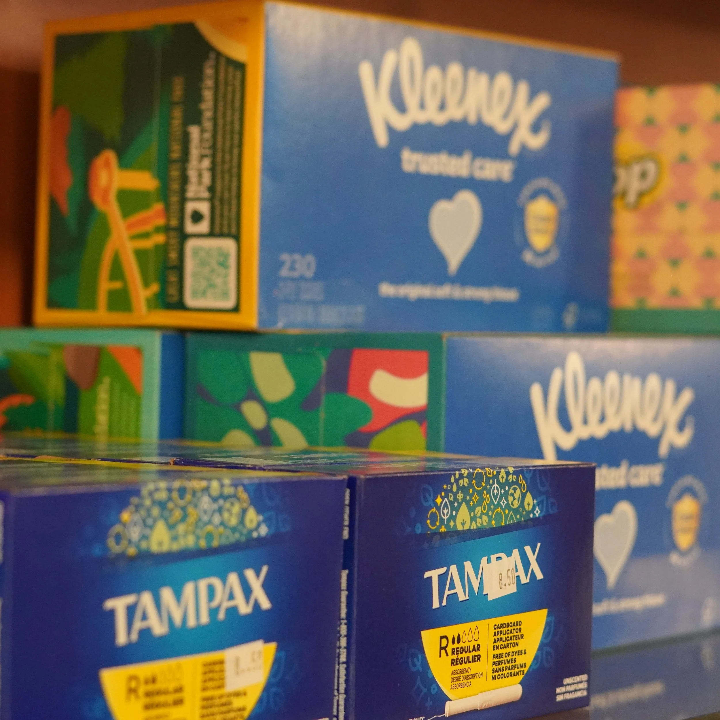 Close-up of Tampax tampon boxes and Kleenex tissue boxes on a shelf.
