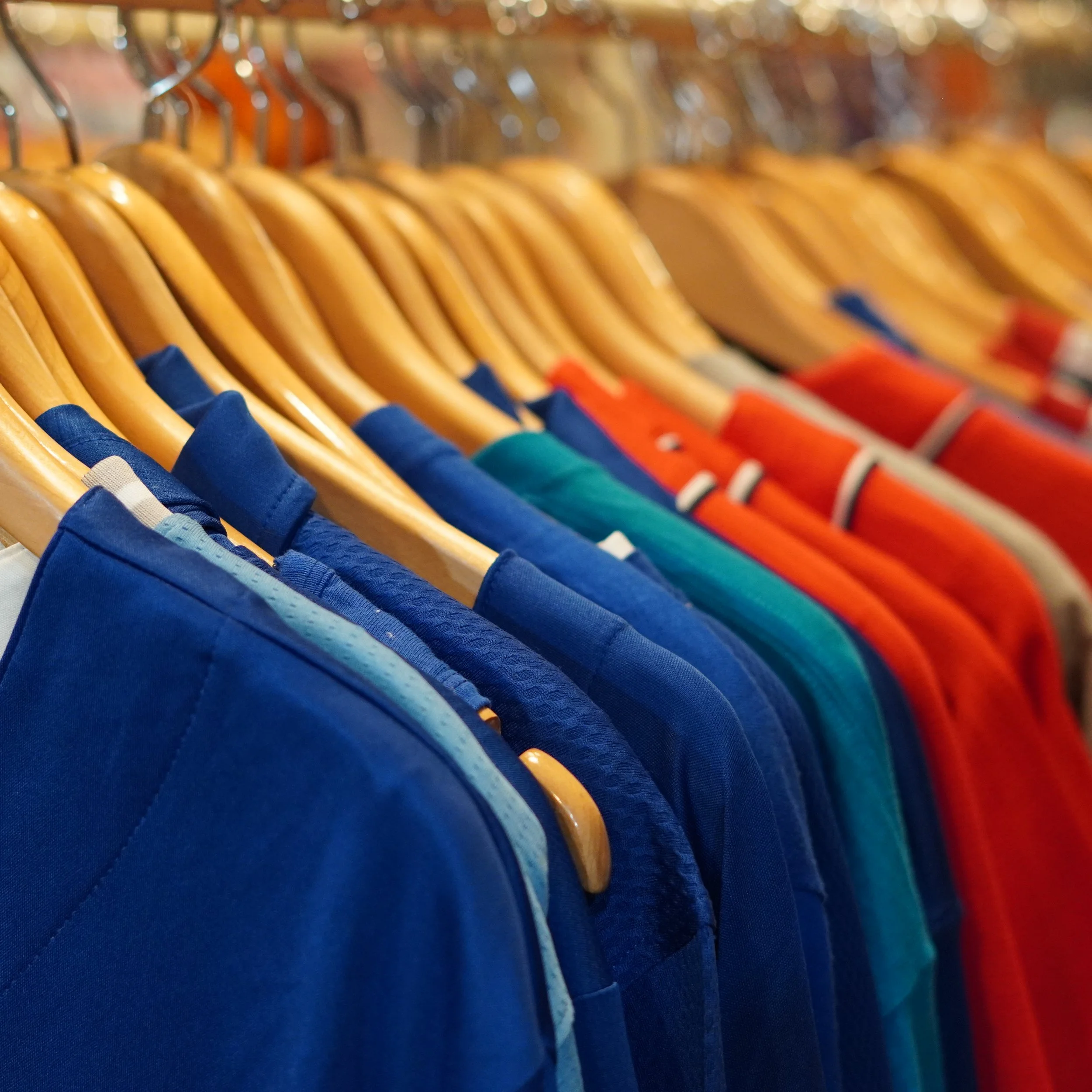A row of colorful T-shirts on hangers, including shades of blue, teal, orange, red, and beige, displayed on a clothing rack available at The French kitchen one-stop shop on 4th floor Westin Bonaventure