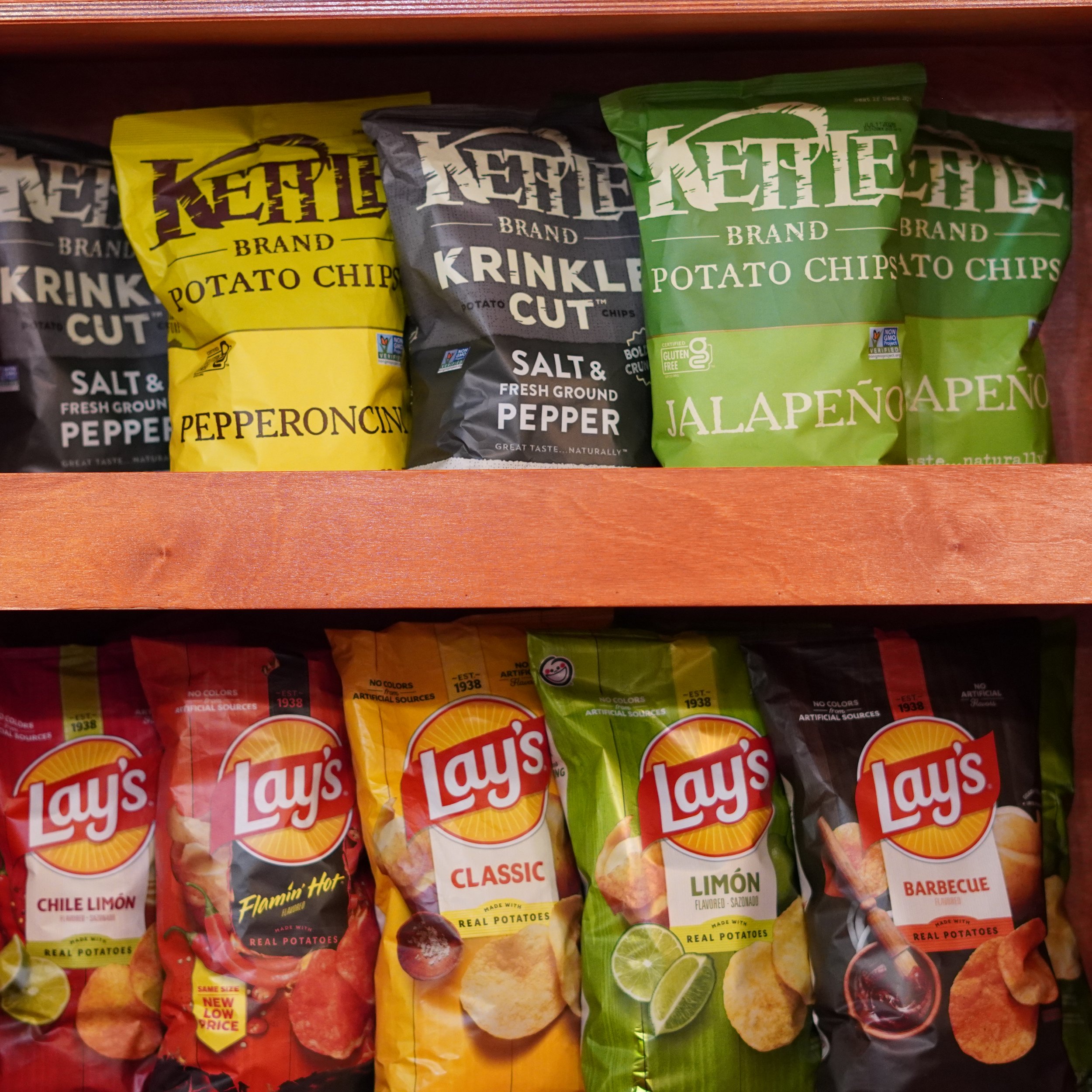 Shelf of various potato chip bags, including Lay's Classic, Lime, Barbecue, and flavored Krinkle Cut chips in different colors available at TheFrench Kitchen, all-in-one store inside the Westin Bonaventure
