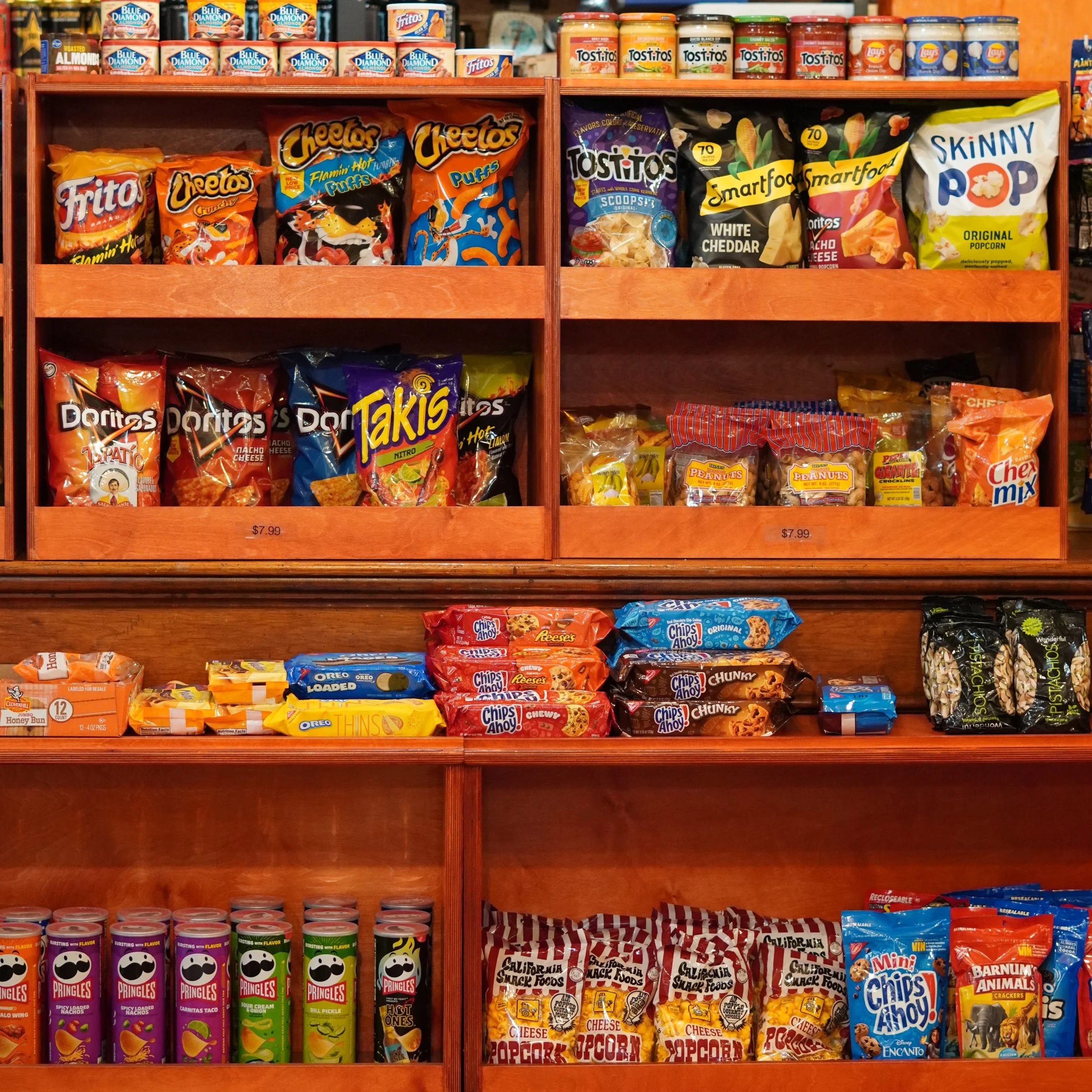 Snack aisle with various chips, popcorn, crackers, and canned goods displayed on wooden shelves available at The French Kitchen, one stop shop in Westin Bonaventure Hotel