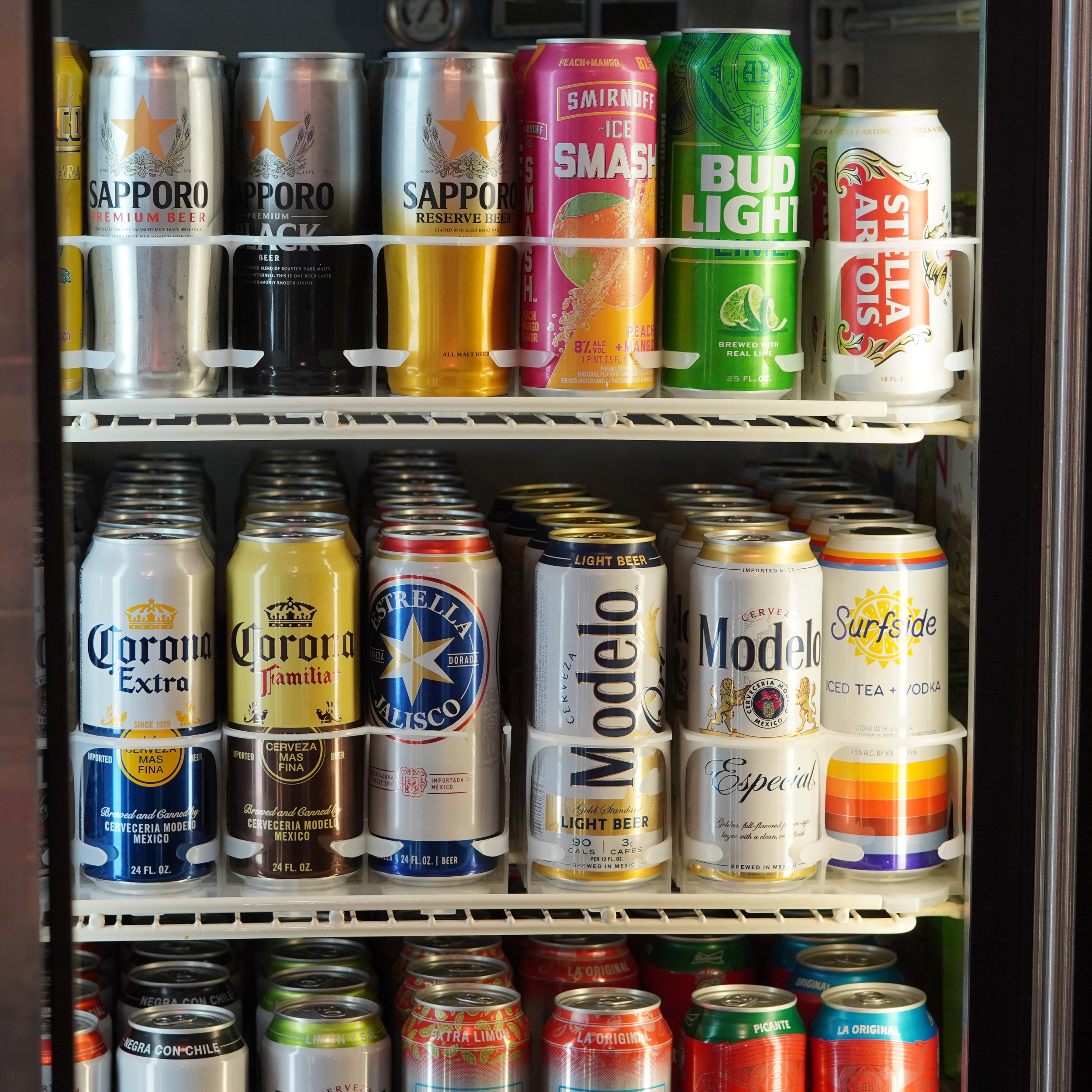 A refrigerator door with shelves filled with various cans of beer and beverages, including Sapporo, Smirnoff Ice Smash, Bud Light Lime, Stella Artois, Modelo, Corona, Surfside, and other brands.
available at The French Kitchen , one-stop shop on 4th 