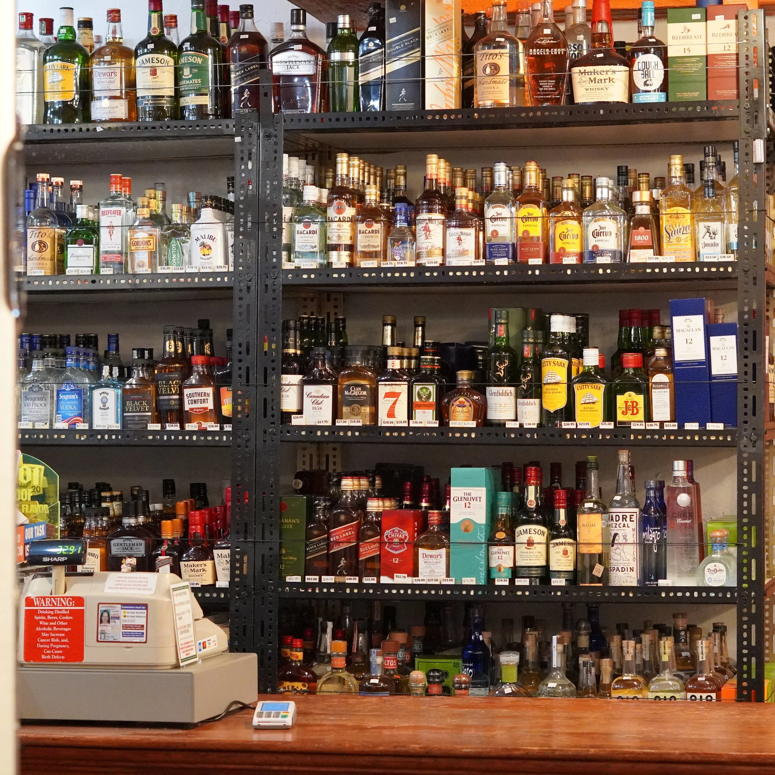 Shelf of various bottles of alcoholic spirits in a liquor store, with a cash register and scale on the counter at the front. of The French Kitchen , one-stop shop on 4th Fllor of The Westin Bonaventure Hotel