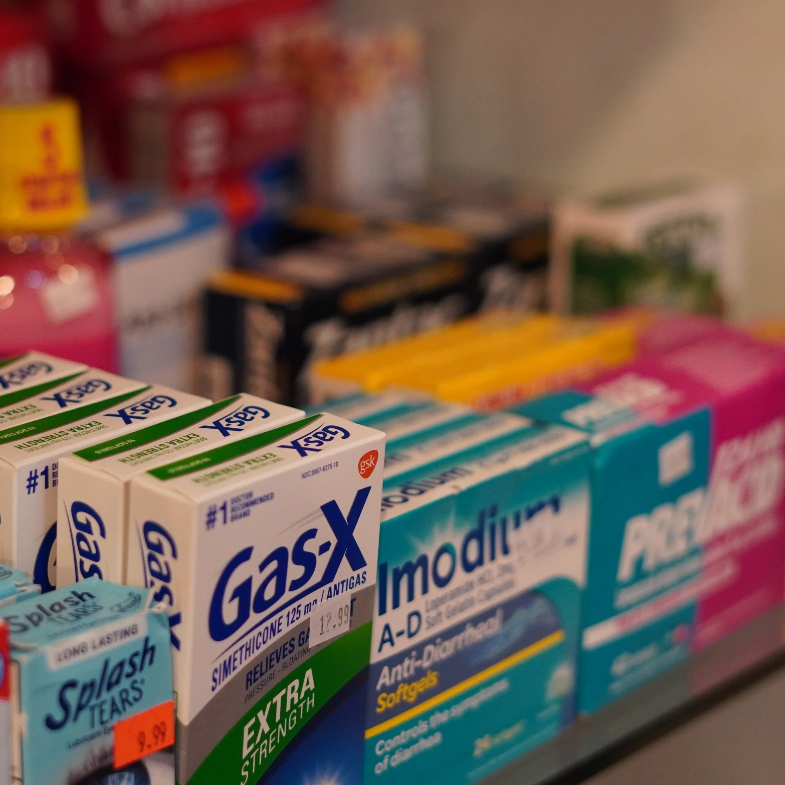 Assorted boxes of over-the-counter medications, including Gas-X, Imodium, and Salash Tears, on store shelves.