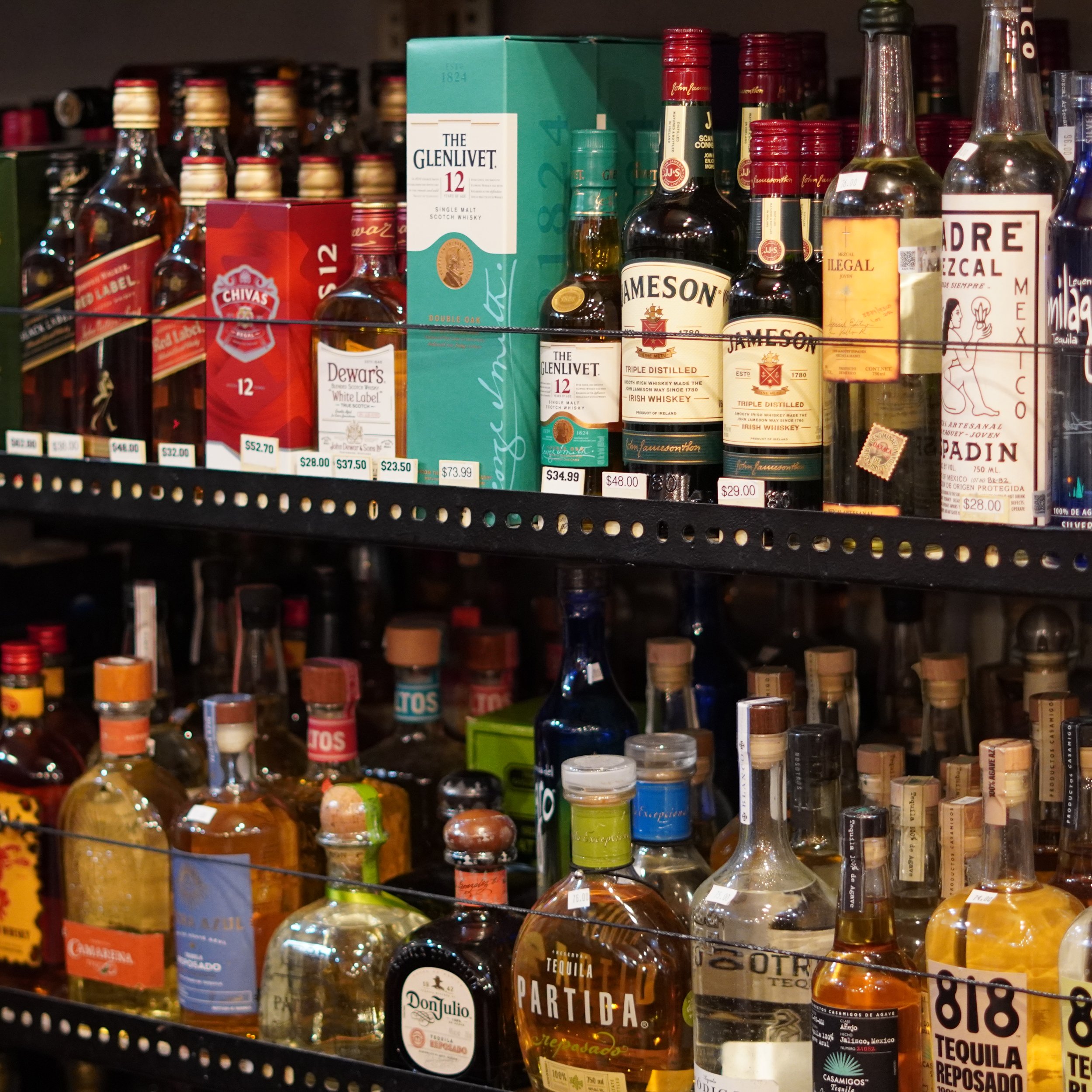 A store shelf filled with bottles of whiskey and other spirits, including brands like Jameson, Glenlivet, and Chivas, with visible price tags.available at The French Kitchen , one-stop shop on 4th Fllor of The Westin Bonaventure Hotel