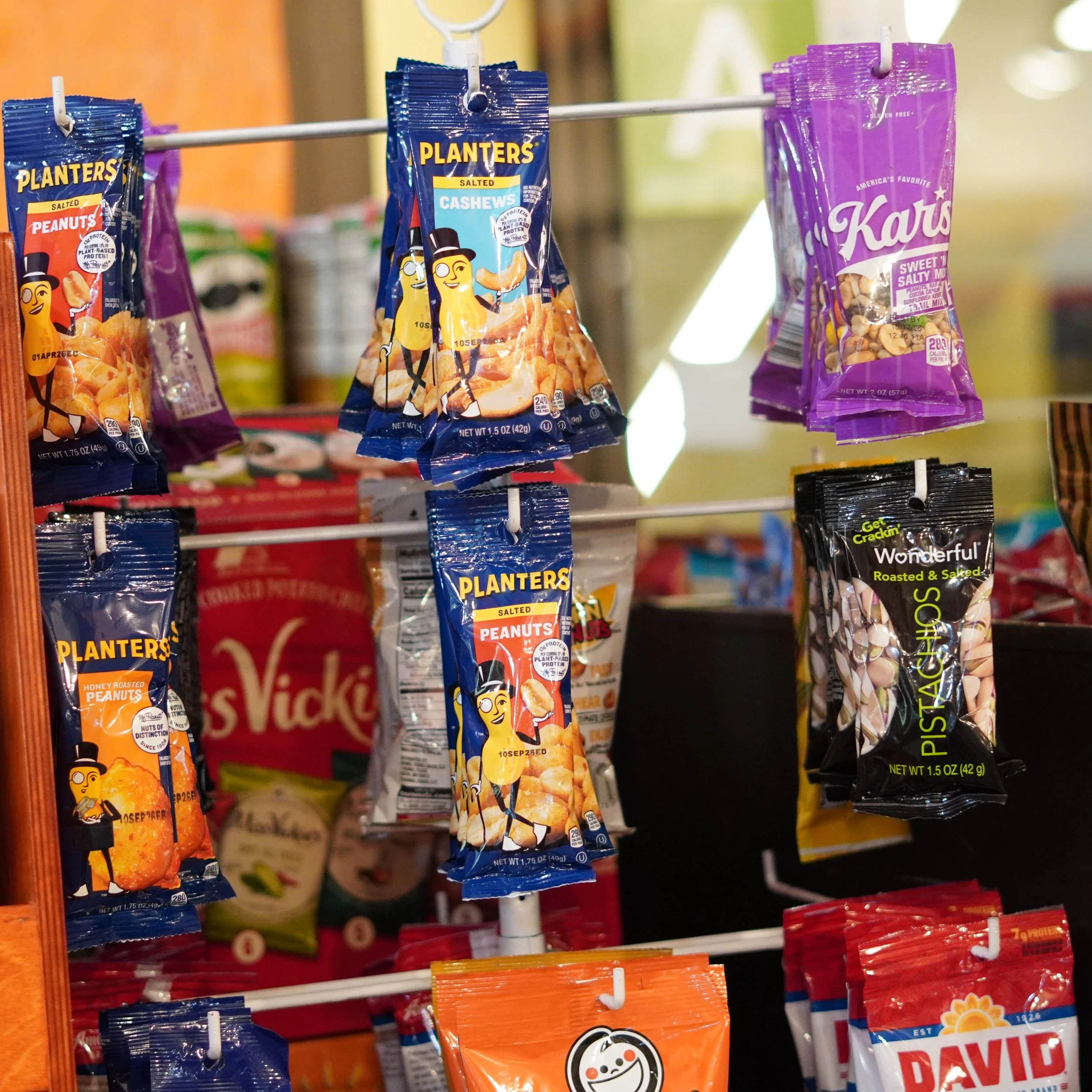Hanging snack packs featuring Planters salted peanuts, honey roasted peanuts, cashews, and pistachios displayed on a store rack available on 4th floor, The French Kitchen your one stop shop inside the Westin Bonaventure