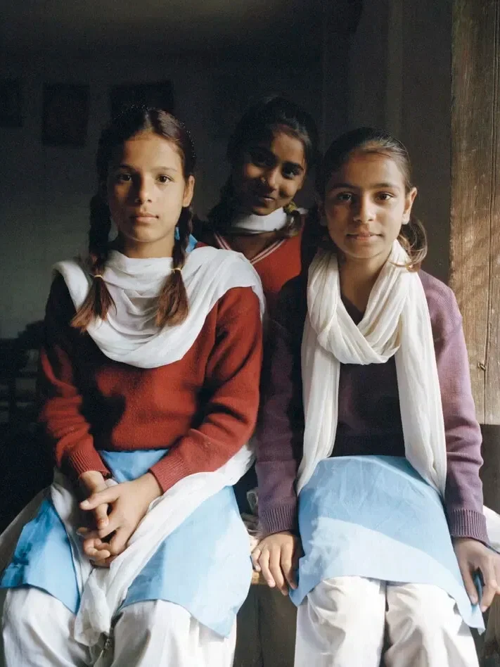 Three young girls with braided hair and matching attire, sitting indoors, facing the camera.