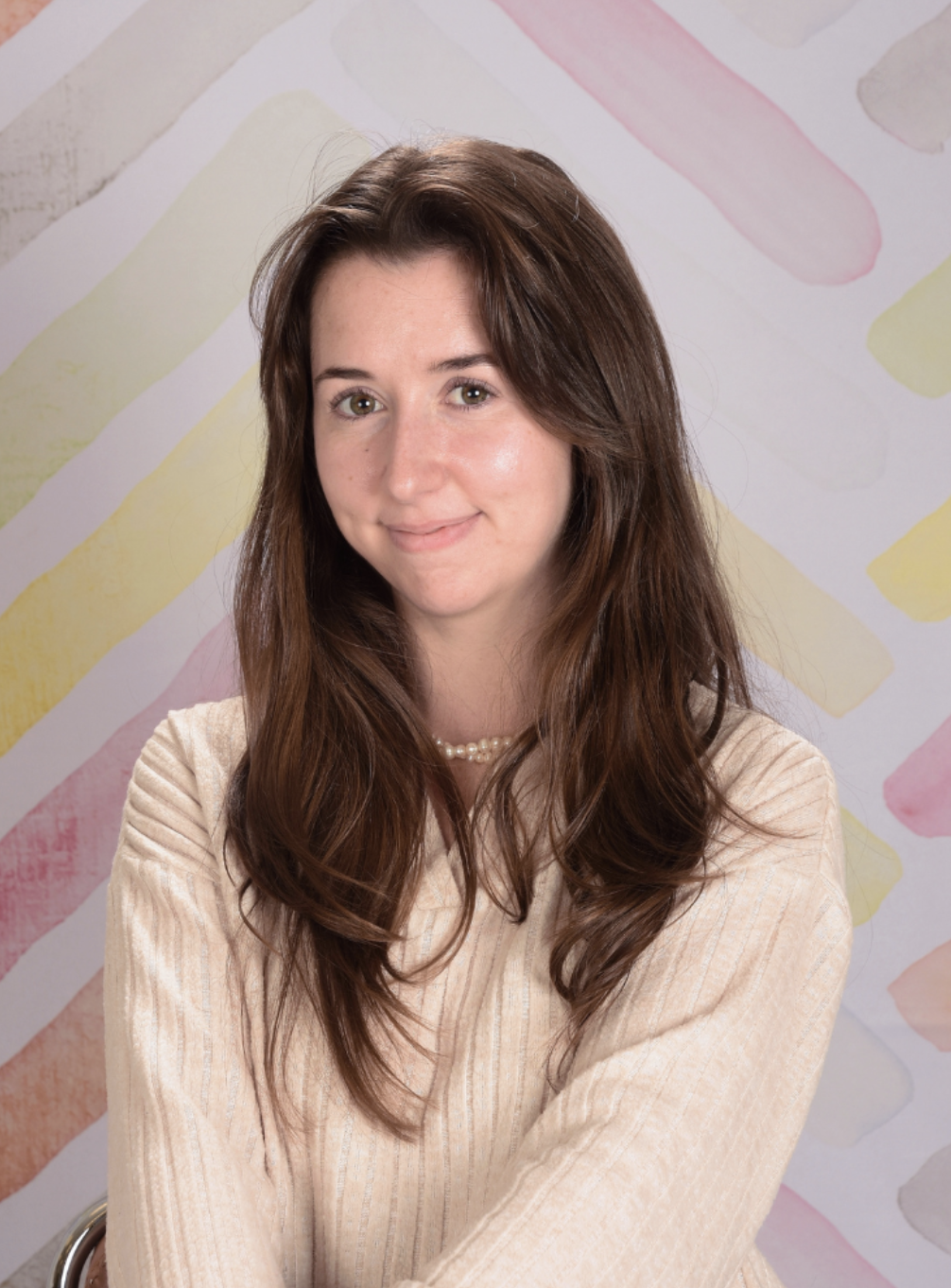 Colleen wearing a beige sweater and pearl necklace, smiling in front of a colorful abstract background.