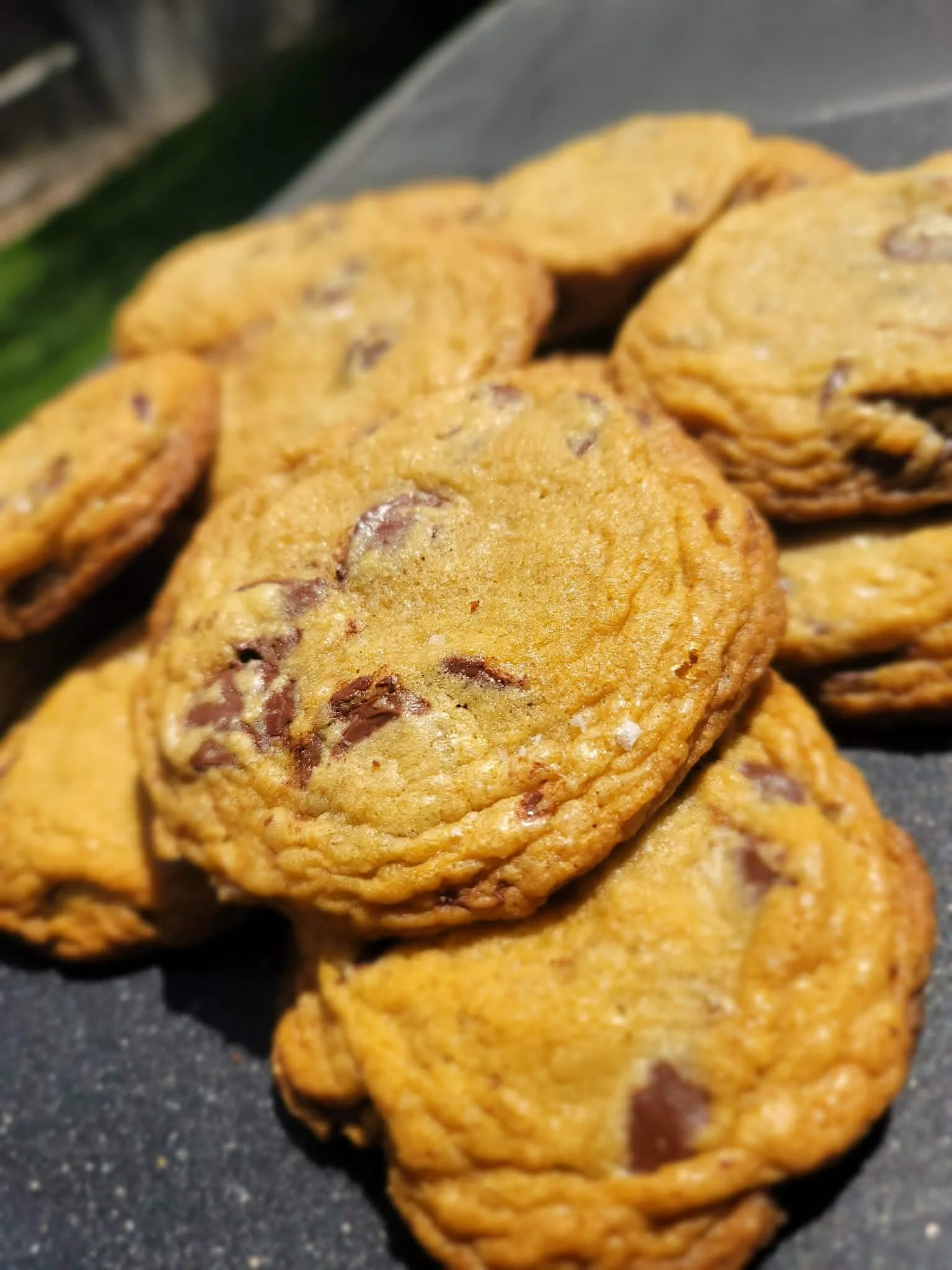 Close-up of chocolate chip cookies stacked on a dark surface.
