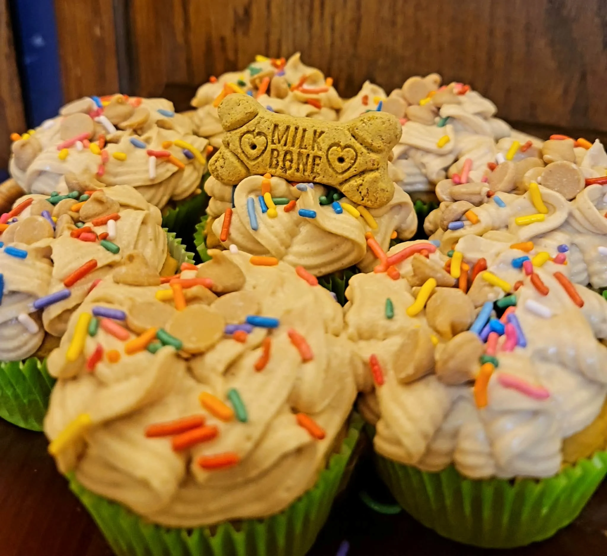 Cupcake decorated with beige frosting, colorful sprinkles, and a dog-shaped biscuit with the words "Milk Bone" on it.